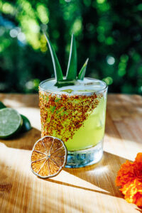 a green cocktail with lime wedge and green tree in background