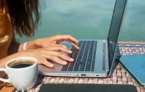 woman working at a laptop by the pool with a cup of coffee