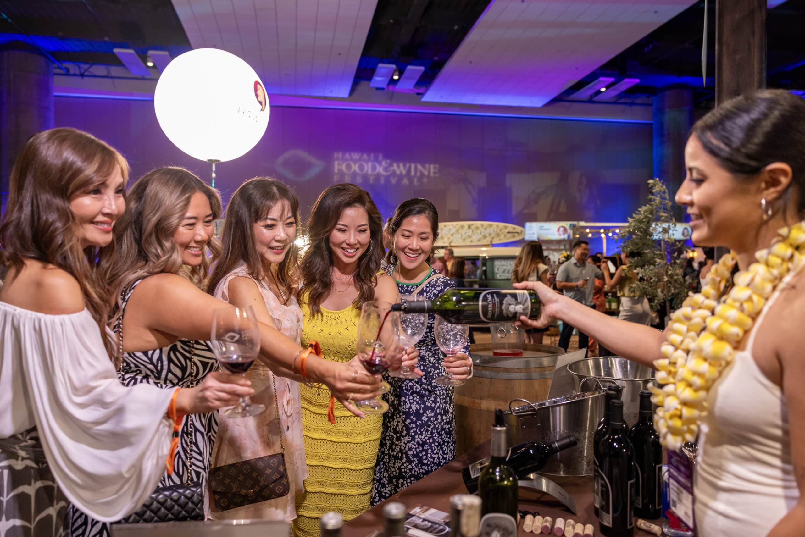 group of women holding out wine glasses while someone pours them wine