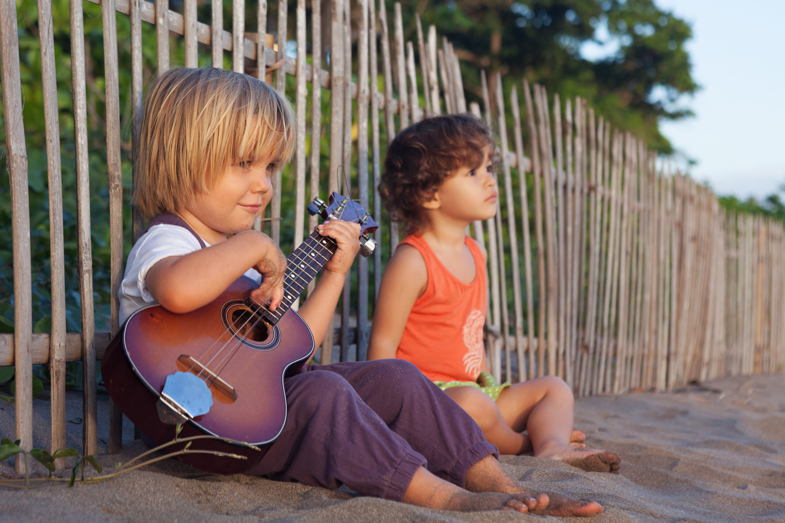 kids playing ukulele on the beach against a fence
