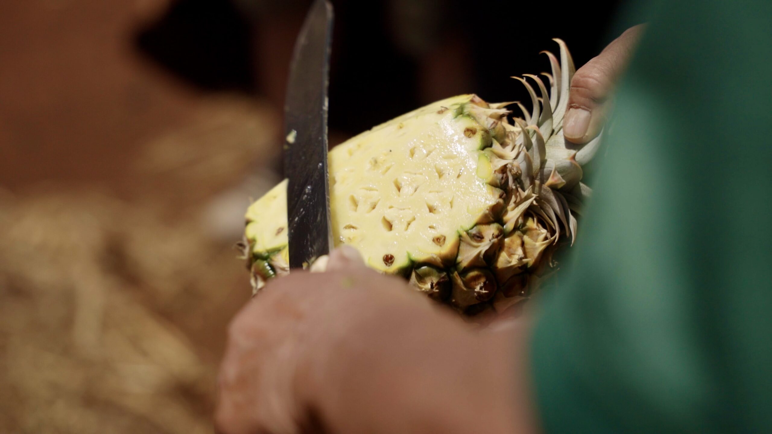 A man slicing the skin off a pineapple.